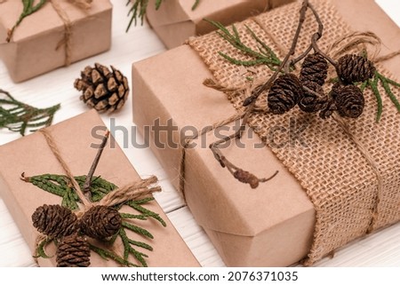 Festive decoration of gifts in eco-style.Gift boxes are wrapped in craft paper,tied with cotton thread,decorated with thuja leaves,cones and burlap.Christmas,New Year and eco-friendly concept.