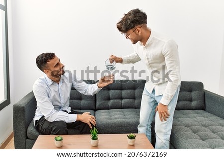 Two hispanic men business workers smiling confident pouring water at office