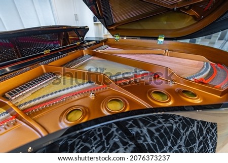 Glossy black grand piano with open lid showing strings ivory keys hammers felts and bench in an elegant room