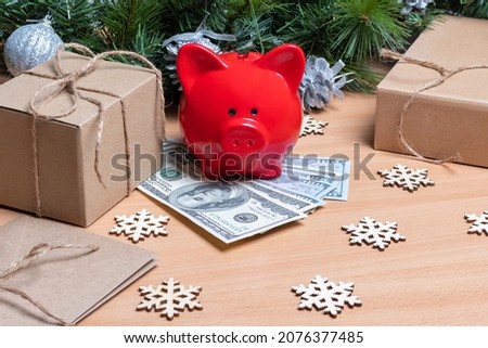 A piggy bank standing on cash dollars on a table with gift boxes, snowflakes and Christmas fir branches.