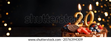Banner with Chocolate birthday cake with berries, cookies and number twenty golden candles on black background, copy space Royalty-Free Stock Photo #2076394309