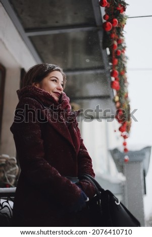 Beautiful woman near Christmas decorated shop on a street uder snowfall, Snowy city