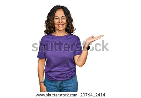 Middle age hispanic woman wearing casual clothes smiling cheerful presenting and pointing with palm of hand looking at the camera. 