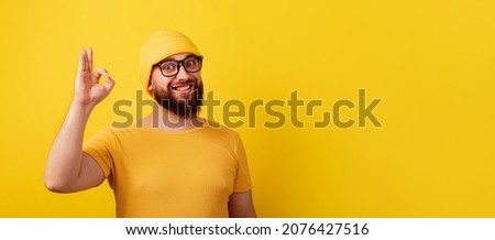 smiling bearded man in glasses showing ok gesture over yellow background, panoramic layout