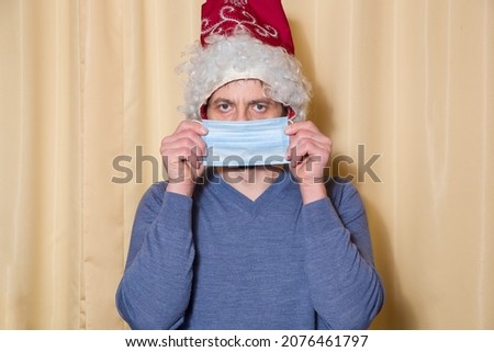 A man wearing a Santa Claus hat covers his face with a medical mask.