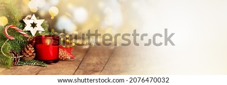 Atmospheric Advent and Christmas decoration with a red candle, wooden star and evergreen fir branches on dark rustic wooden planks, wide panoramic format, copy space,banner. Royalty-Free Stock Photo #2076470032