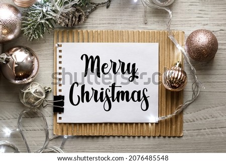Notepad on the table with the text Merry Christmas. Christmas background with decorations from balls and garlands. Delicate shades. Christmas or festive concept.