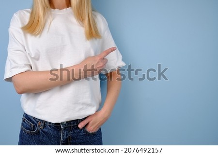 Woman in a white T-shirt poses near a blue wall. Hand gestures and emotions. Studio photography. The concept of emotion, strength and fun. Casual wear. Space for inscriptions and logo
