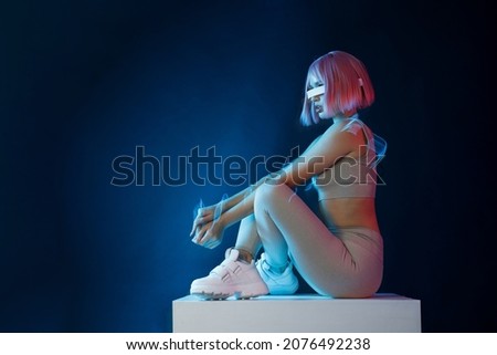 Woman in futuristic costume. Female posing in glasses of virtual reality. Augmented reality game, future technology, AI concept. VR. Neon blue and red light. Dark background.