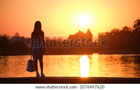 Young woman in casual outfit relaxing on lake side on warm evening. Summer vacations and travelling concept.