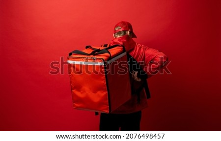 Delivery man in red uniform with a thermal backpack isolated on a white background. Fast home delivery. Online order. Courier delivers groceries home. Royalty-Free Stock Photo #2076498457