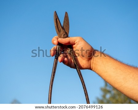 Close-up of a man's hand holding an old rusty metal scissors. Blurred background