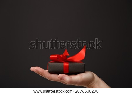 Woman's hand holding black gift box with red bow over black background. Black friday sale, Christmas sale, discount concept. Valentine's day. Father's day
