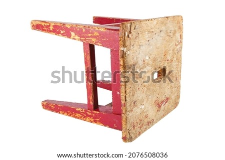 Old used wooden stool with peeling red paint laid on its side. Loft style chair isolated on a white background.