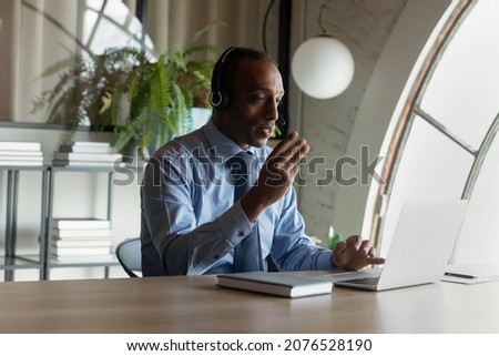 Concentrated young African American businessman coach in headset mentoring colleagues online, holding distant video call meeting or sharing knowledge distantly using computer app in modern boardroom. Royalty-Free Stock Photo #2076528190