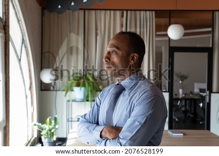 Thoughtful young African American businessman employee worker in formal wear standing near window looking at camera, considering difficult problem solution, new challenges or career opportunities. Royalty-Free Stock Photo #2076528199
