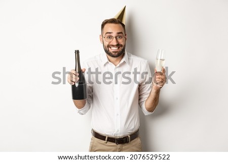 Celebration and holidays. Happy birthday guy enjoying b-day party, wearing funny cone hat and drinking champagne, white background