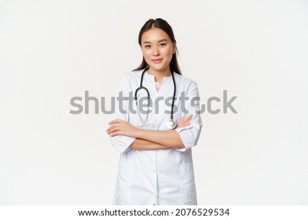 Image of confident female doctor, intern with stethoscope and medical robe, cross arms like professional, looking confident at camera, white background Royalty-Free Stock Photo #2076529534