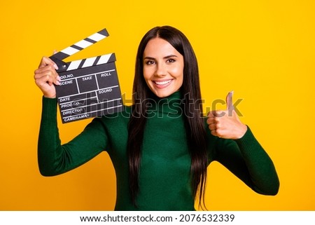 Photo of brown haired young woman make thumb-up hold clapboard smile movie maker isolated on yellow color background