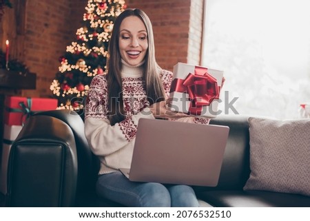 Portrait of attractive cheerful woman sitting on divan calling web showing giftbox eve advent at loft interior home indoors Royalty-Free Stock Photo #2076532510