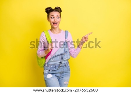 Photo of cute impressed young woman wear denim overall rucksack pointing empty space isolated yellow color background