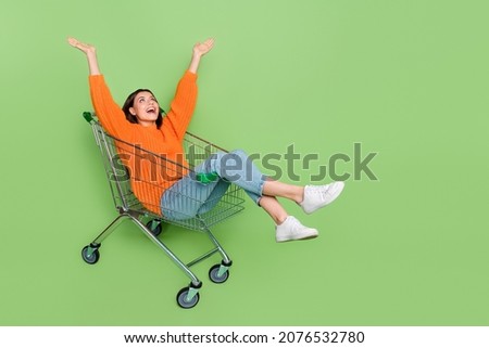 Full length photo of crazy lady ride push cart raise arms up amazed autumn bargain isolated over green color background Royalty-Free Stock Photo #2076532780