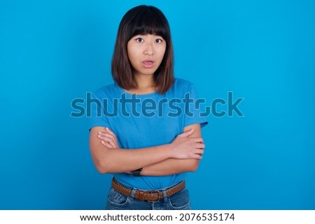 Shocked embarrassed young asian woman wearing blue t-shirt against blue background keeps mouth widely opened. Hears unbelievable novelty stares in stupor