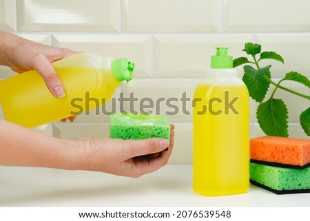 Woman pours dish detergent onto a sponge. Detergent bottle for dishes with mint and orange. Luminous aroma. spring-cleaning. Housewife uses dishwashing detergent for wash up dishes in the kitchen Royalty-Free Stock Photo #2076539548