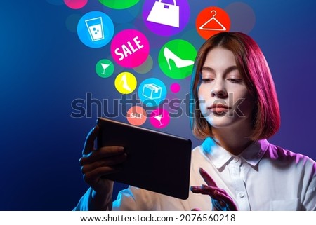 Woman with a tablet is engaged in online shopping. She buys goods online. Girl with many icons buys goods on tablet. Student is engaged in online shopping. Girl purchases goods through application