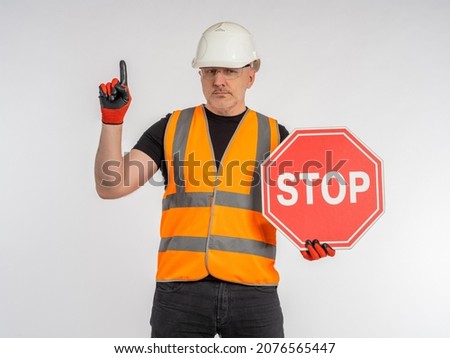 Builder warns of danger. Stop sign in hand of male builder. Concept - approaching place of repair or construction. No trespassing sign. Sign with inscription STOP. Frowned builder on light background