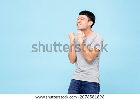 Happy ecstatic young Asian man raising his fists doing yes gesture celebrating success in isolated light blue studio background Royalty-Free Stock Photo #2076581896