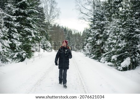 Teenage boy walks through a snowy forest on a cold winter day with a hot drink in a thermos. Healthy lifestyle. Useful activity.