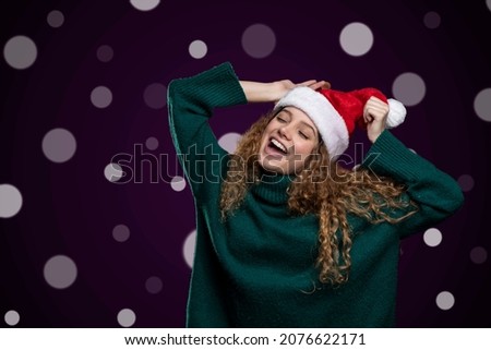 young woman making happy expressions wearing santa hat and christmas sweater, with lights in the background