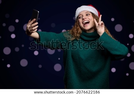 woman in sweater and christmas hat making love and peace sign while taking a selfie