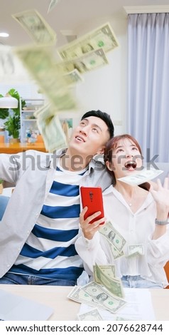 asian excited young couple looking up and shouting from happiness while money rain falling from above at home