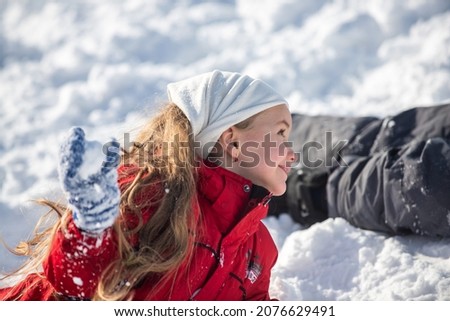 Funny excited child girl face in snow on winter outdoor. Children in winter outdoor in frost snowy day. Amazed kid resting together in park with winter background. Expressive kids emotions.