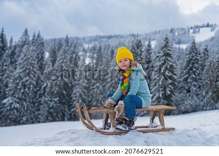 Funny boy having fun with a sleigh on winter landscape. Cute children playing in a snow on snowy nature landscape. Winter activities for kids.