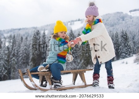 Boy and girl kids sliding with sledge in the snow. Active winter children outdoors. Kids playing in the winter forest.