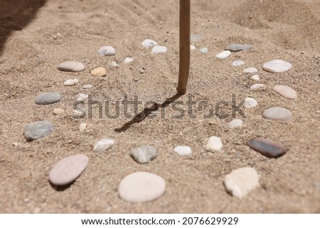Wooden stick and pebbles on sand showing time by shadow Royalty-Free Stock Photo #2076629929