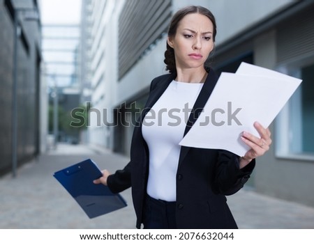 Serious woman is dissatisfied of the results of the financial report outdoors.