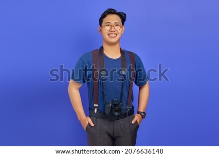 Cheerful and excited handsome photographer holding a professional camera on purple background