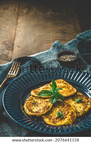 Small pancakes with herbs on a blue plate on rustic wooden background, vertical with copy space