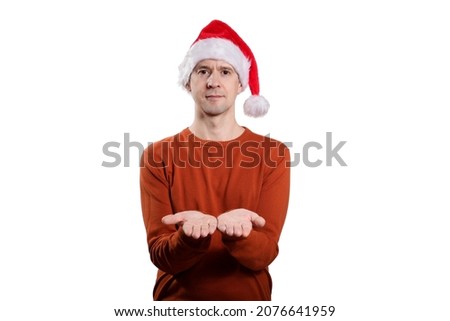 An isolated shot of an adult man in a Christmas cap, an orange sweater. He holds the palms of his hands parallel to the floor, looks into the camera. On a white 