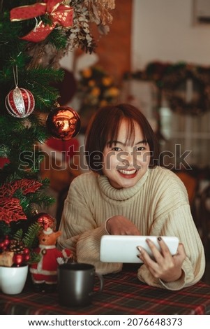 Young smiling woman looking on a tablet with christmas tree in background.