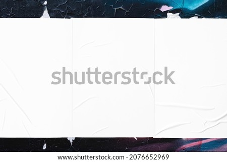 Closeup of colorful messy painted urban wall texture with three wrinkled glued poster templates. Modern mockup for design presentation. Creative urban city background. 
