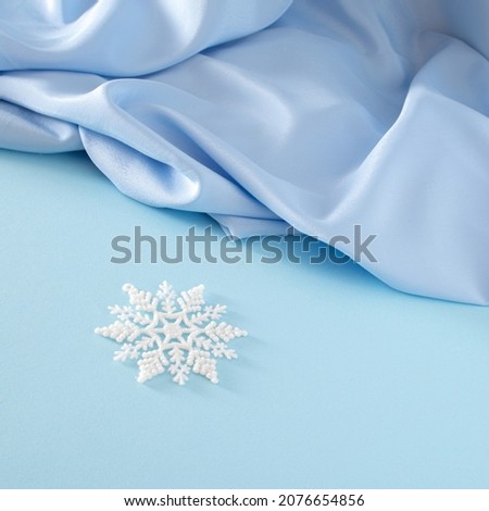 Modern creative Christmas composition with white snowflake on pastel blue background against shiny blue curtain. Creative New Year concept with copy space.