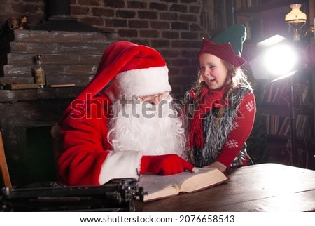 Santa Claus and elf with a sweet smile whispers Santa Claus in his ear sitting at a huge wooden table for the New Year and Christmas 2022