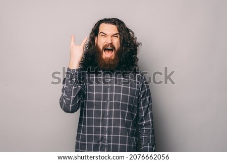 Photo of handsome bearded man showing rock sign and screaming over grey background