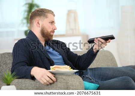 unemployed man watching tv and eating a sandwich