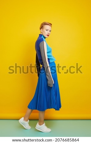 Fashion model in blue trendy sweater, blue skirt and white sneakers. Studio shot.